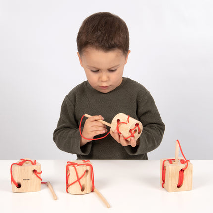 kind speelt met Tickit 4 houten rijgblokken